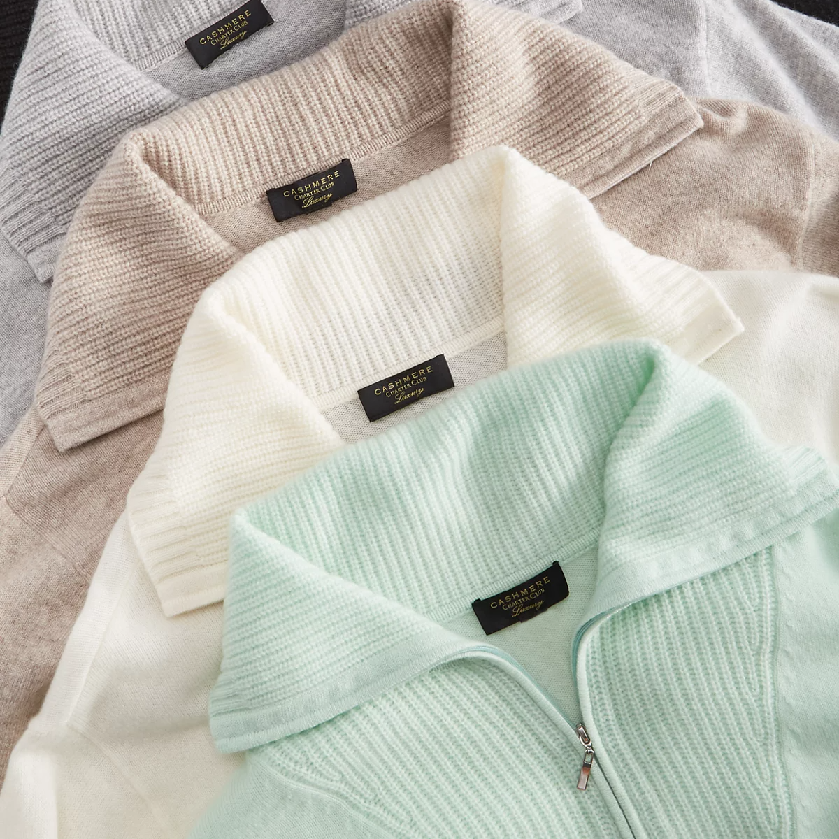 Four cashmere sweaters in pastel gray, beige, white, and mint colors are displayed with ribbed collars and labeled \“Cashmere.\“