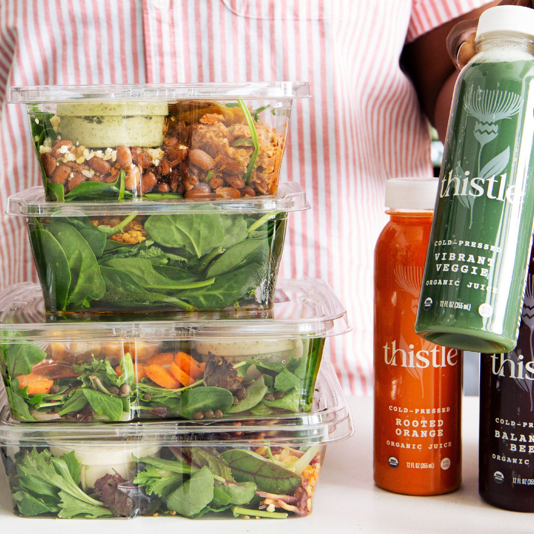 Stack of salad containers and bottles of Thistle cold-pressed organic juices, including \“Vibrant Veggie,\“ \“Rooted Orange,\“ and \“Balanced Beet.\“