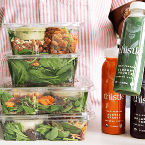 Stack of salad containers and bottles of Thistle cold-pressed organic juices, including \“Vibrant Veggie,\“ \“Rooted Orange,\“ and \“Balanced Beet.\“