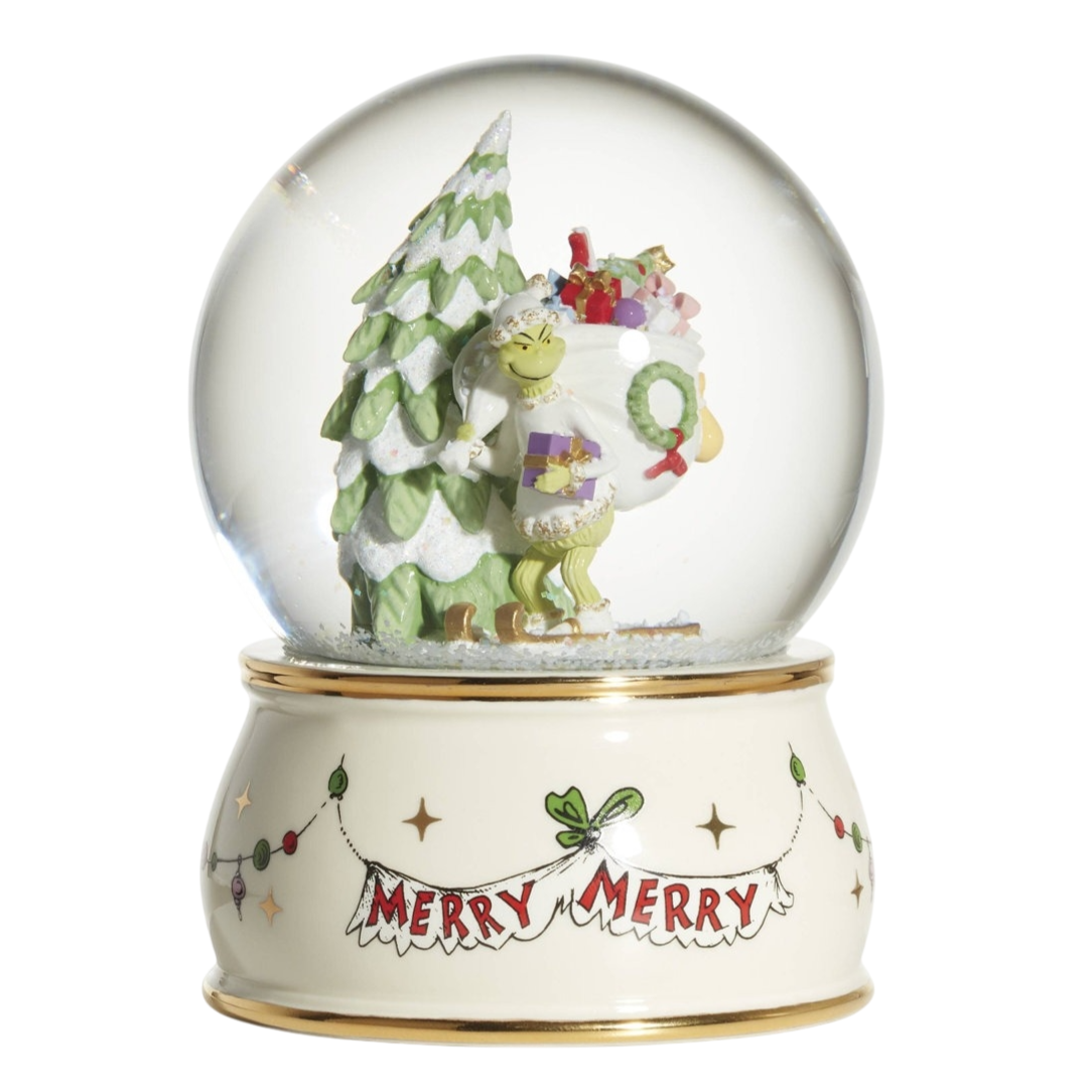 A snow globe depicting a green character with a Christmas tree and sack of gifts, on a base with \“Merry Merry\“ text and decoration.