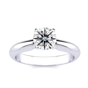 A solitaire ring featuring a 1-carat round diamond set in a simple, polished metal band with a classic four-prong setting. The band has a smooth, reflective finish, enhancing the diamond's brilliance.