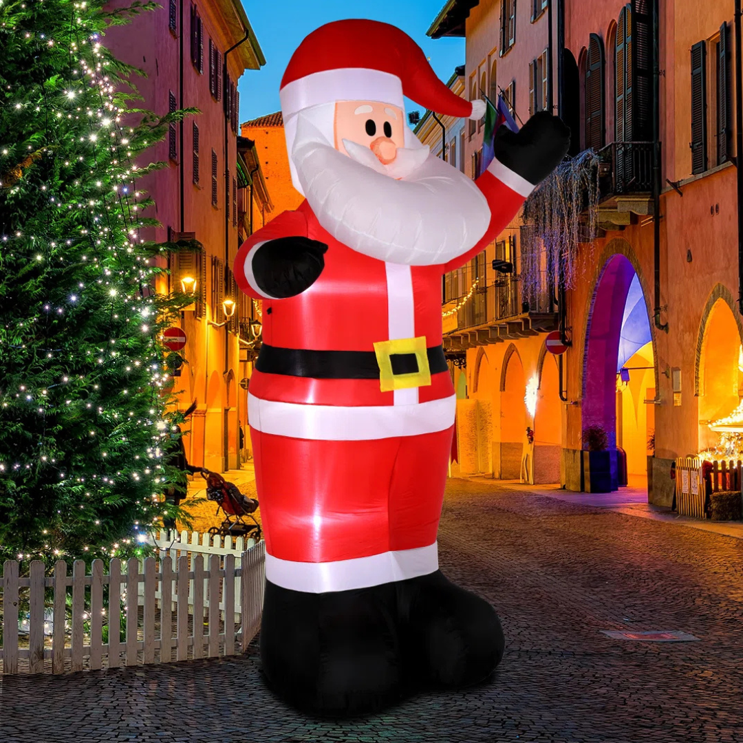 A large inflatable Santa Claus stands cheerfully beside a decorated Christmas tree in a festive street scene.