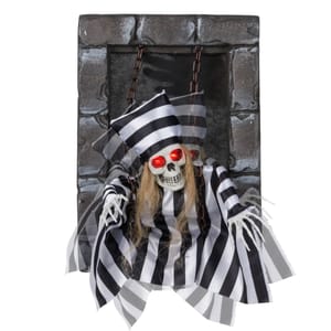 Hanging skeleton decoration with red glowing eyes, dressed in a black and white striped outfit and hat, set in a stone-like frame with chains.