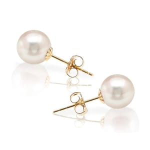 A pair of pearl earrings with gold posts and backs on a reflective surface.