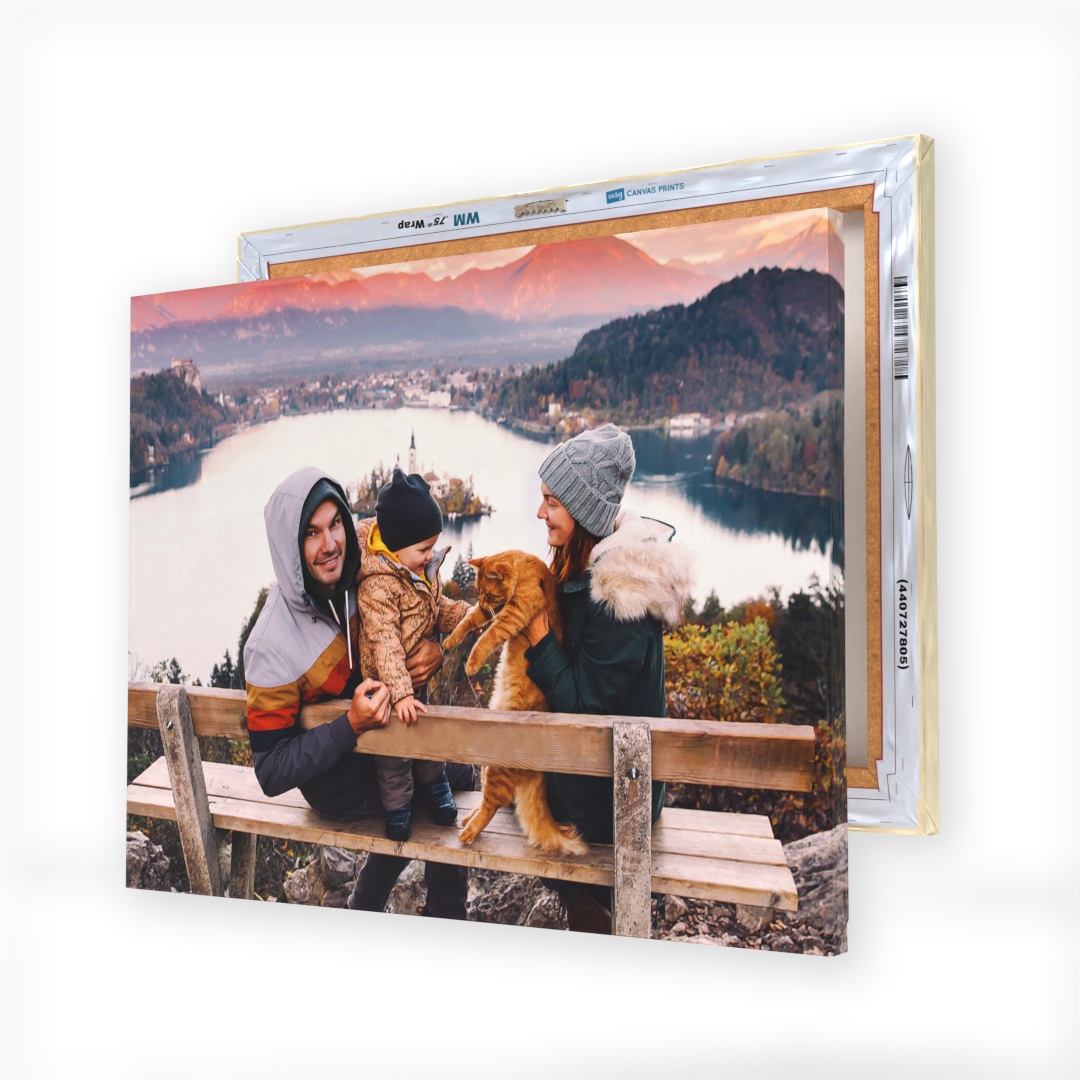A canvas print displays a family with a child and cat enjoying a scenic lake and mountain view, mounted on a wooden bench.