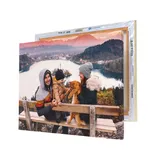 A canvas print displays a family with a child and cat enjoying a scenic lake and mountain view, mounted on a wooden bench.