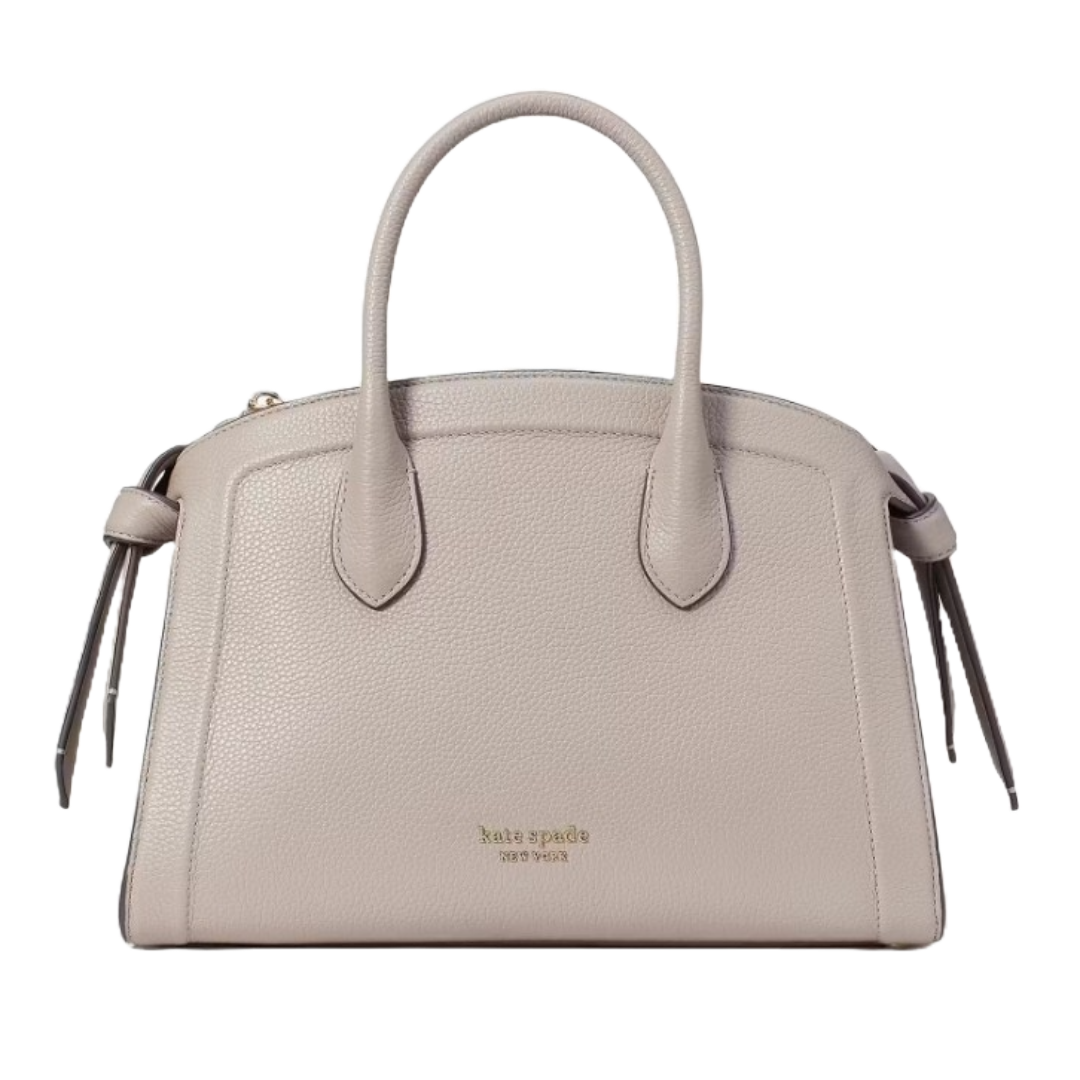 A taupe Kate Spade Zip-Top Leather Satchel with dual handles, pebbled texture, and side tassel details. It features the brand's logo on the front, offering a classic and elegant look.