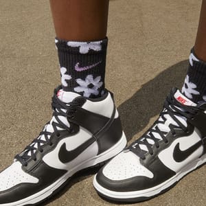 A person is wearing black and white high-top sneakers with the Nike logo, paired with black and white patterned Nike socks.