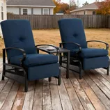 Two blue cushioned recliner chairs with black metal frames are positioned on a wooden deck, separated by a small table holding a white cup and saucer.