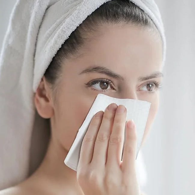 A woman is using a facial cleansing wipe on her face.