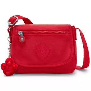 A red Kipling crossbody bag with a zippered front pocket, adjustable strap, and attached fuzzy keychain charm.