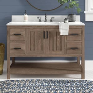 The Sand & Stone Marissa Vanity features a rustic wood design with four side drawers and two center cabinet doors, complemented by a white countertop and a dark faucet. It includes a lower shelf for additional storage, set against a blue shiplap wall.