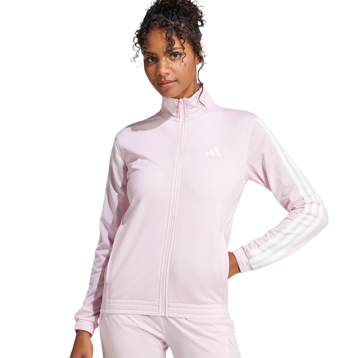A woman wearing a light pink Adidas tracksuit with white stripes on the sleeves and legs, featuring a full-zip jacket and matching pants.
