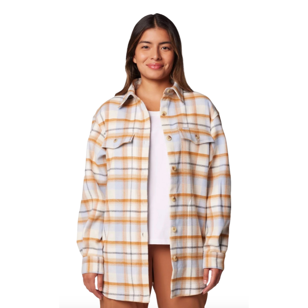 A woman is wearing a check-patterned flannel shirt-jacket in shades of beige, light blue, and white over a white top and tan pants. The jacket features button closures and chest pockets.