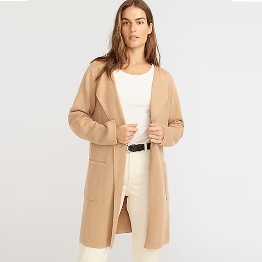 A woman is wearing a beige long cardigan over a white top paired with an off-white skirt or pants.