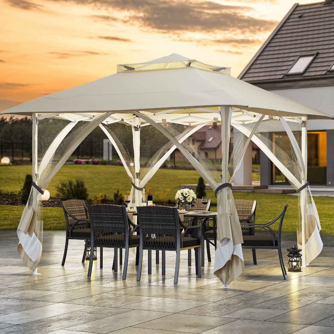 A stylish outdoor canopy with a table and chairs set, featuring a metal frame and fabric roof, surrounded by a landscaped patio and garden at sunset.