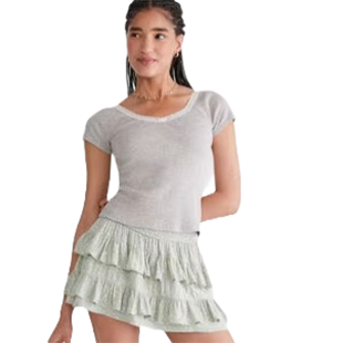 A woman wearing a light gray short-sleeve top paired with a light green tiered ruffle skirt.