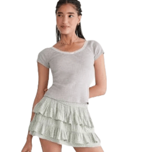 A woman wearing a light gray short-sleeve top paired with a light green tiered ruffle skirt.