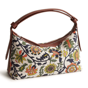 A handbag with a curved brown handle features a colorful floral pattern on a white background, incorporating yellow, red, green, and black designs.