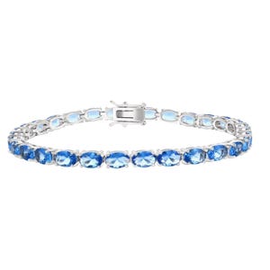 A sleek silver tennis bracelet featuring a row of oval-cut blue gemstones, set in prongs with a secure clasp.