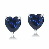 A pair of heart-shaped sapphire stud earrings set in a prong setting with a reflective surface beneath.