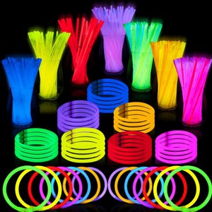 Assorted colorful glow sticks are displayed, arranged in groups of bracelets, necklaces, and straight sticks, reflecting on a black surface.