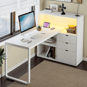 A modern white desk features a monitor, keyboard, and mouse, with storage drawers and shelving. An LED-lit surface hosts a tablet and books, next to a small plant and a decorative fan.