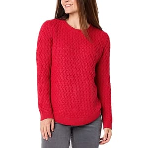 A woman is wearing a red textured sweater with a scoop neckline and long sleeves, paired with gray jeans.
