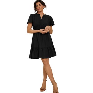 A woman is wearing a black dress with short sleeves, an elastic waistband, and a ruffled hem, paired with light brown ankle-strap sandals.