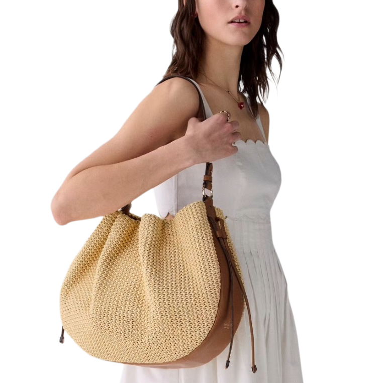 A woman in a white dress holds a large woven tote bag with leather straps.