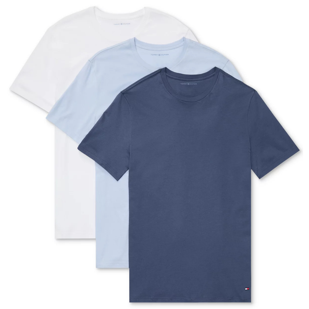A set of three Tommy Hilfiger t-shirts in solid colors: navy, light blue, and white. They feature a classic crew neck and a small logo on the lower left hem.