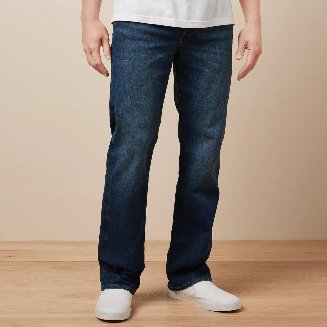 A person wearing blue denim jeans and white slip-on shoes.