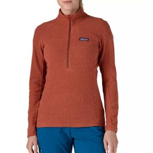 Patagonia R1 Pullover is a women's rust-colored fleece with a textured pattern, featuring a quarter-zip closure and a small chest logo patch, paired with blue pants.