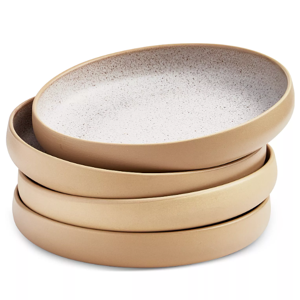 A stack of four round, beige ceramic plates with a slightly speckled white interior surface.