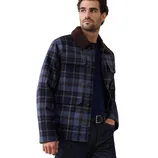 A man is wearing a blue and black plaid jacket with a brown collar, paired with a navy shirt and dark jeans.