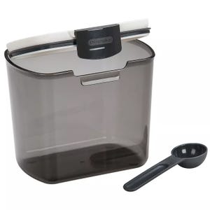 Opaque gray coffee storage container with a hinged lid for secure sealing, featuring a small tab for easy opening. Accompanied by a matching dark measuring scoop designed for convenient coffee portioning.