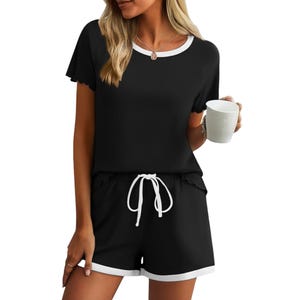 A woman wearing a black loungewear set with white trim and drawstring, holding a white cup.