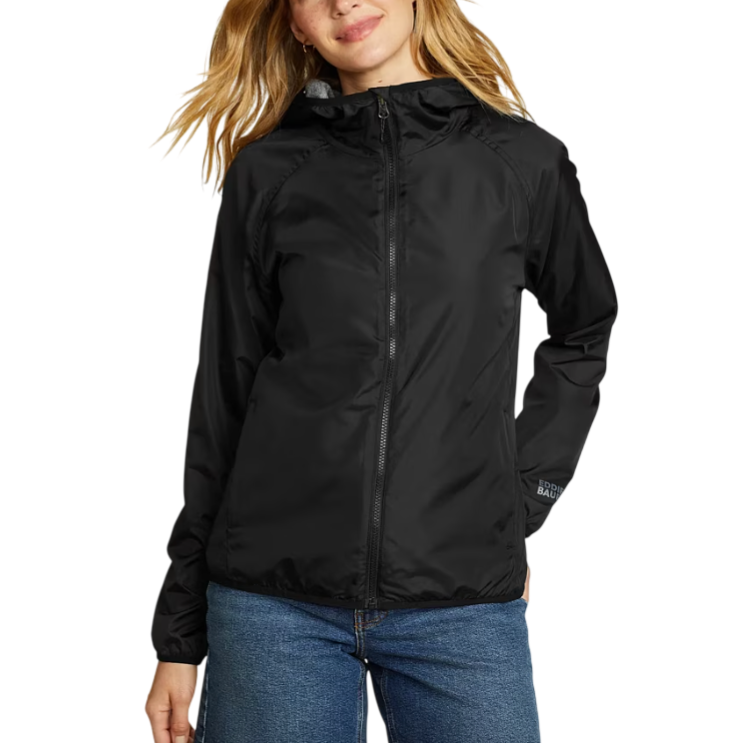 A woman is wearing a black hooded jacket with a front zipper, paired with blue jeans. The jacket is from Eddie Bauer, featuring a simple, functional design.