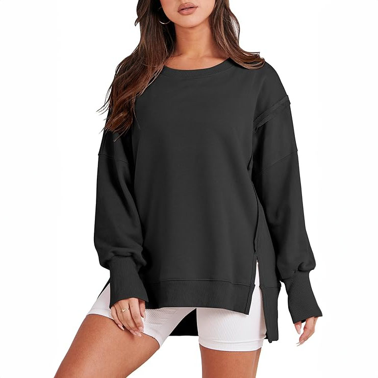 A woman is wearing a black oversized sweatshirt with drop shoulders and ribbed cuffs, paired with white shorts.