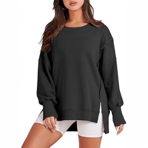 A woman is wearing a black oversized sweatshirt with drop shoulders and ribbed cuffs, paired with white shorts.