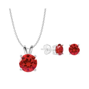 A jewelry set featuring a silver chain necklace with a round red gemstone pendant and matching round red gemstone stud earrings.