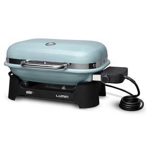 Electric grill with a light blue cover, featuring a black base, handle, and a flexible power cord on the right side. Brand name: Weber Lumin.