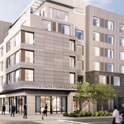 A modern building with \“AC Hotel Ann Arbor\“ signage, featuring multiple stories, large windows, and a rooftop area with people.