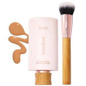 Tarte Timeless Hydrating Foundation is displayed with a bamboo-handled brush, featuring a thick liquid formula and a light pink packaging with rose gold accents.