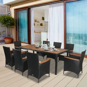 A patio dining set with a rectangular wooden table and six wicker chairs, set up on a balcony.
