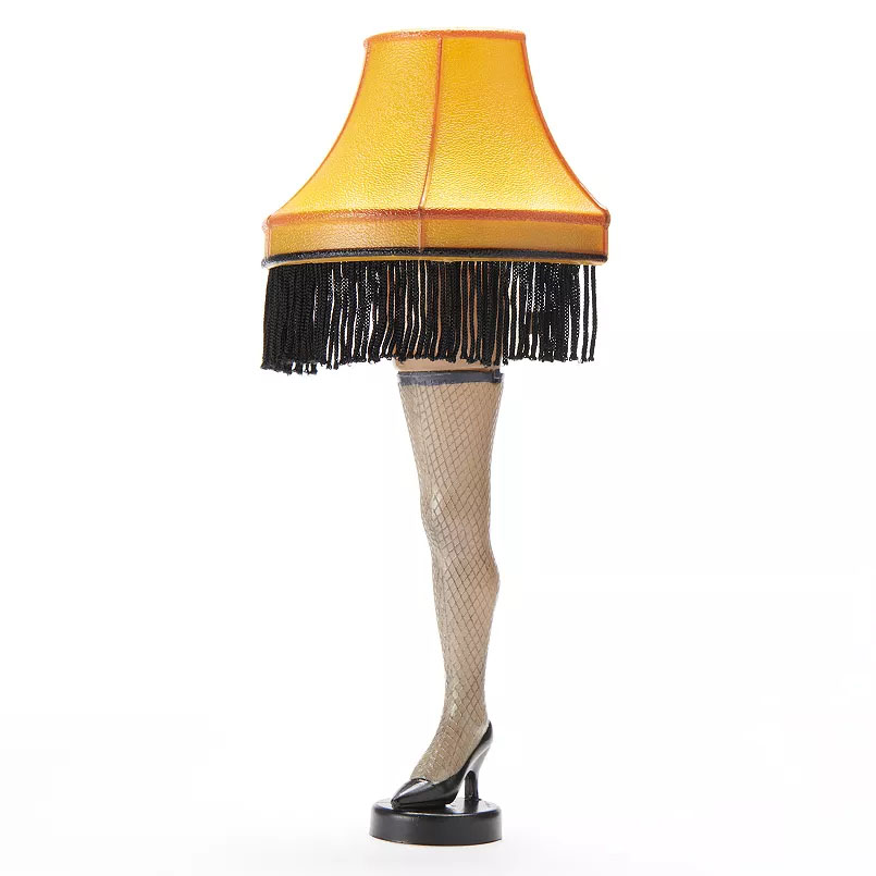 A festive lamp shaped like a woman's leg in a high heel and fishnet stocking, topped with a fringed, yellow lampshade.