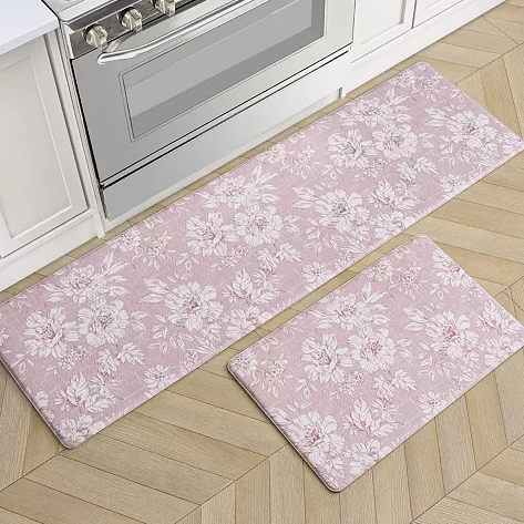 Two floral-patterned kitchen mats in shades of pink are placed in front of an oven; one is long and rectangular, while the other is shorter and wider.