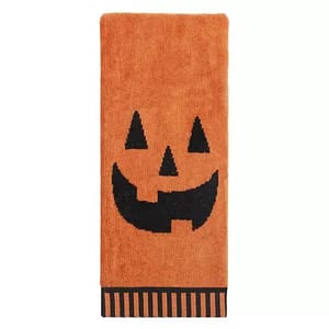 Orange hand towel with a black jack-o'-lantern face design and a striped border at the bottom.