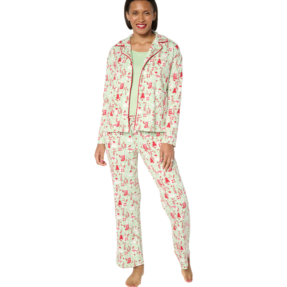 A woman is wearing a pajama set with a red holiday-themed print featuring various festive elements. The set includes a button-up top and matching pants, paired with a green undershirt.