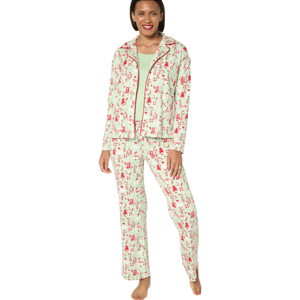 A woman is wearing a pajama set with a red holiday-themed print featuring various festive elements. The set includes a button-up top and matching pants, paired with a green undershirt.